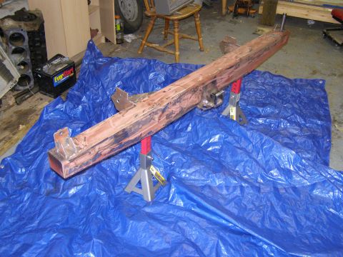 1993 Ford Bronco - A disassembled vehicle frame component is supported by jack stands on a blue tarp in a garage setting.