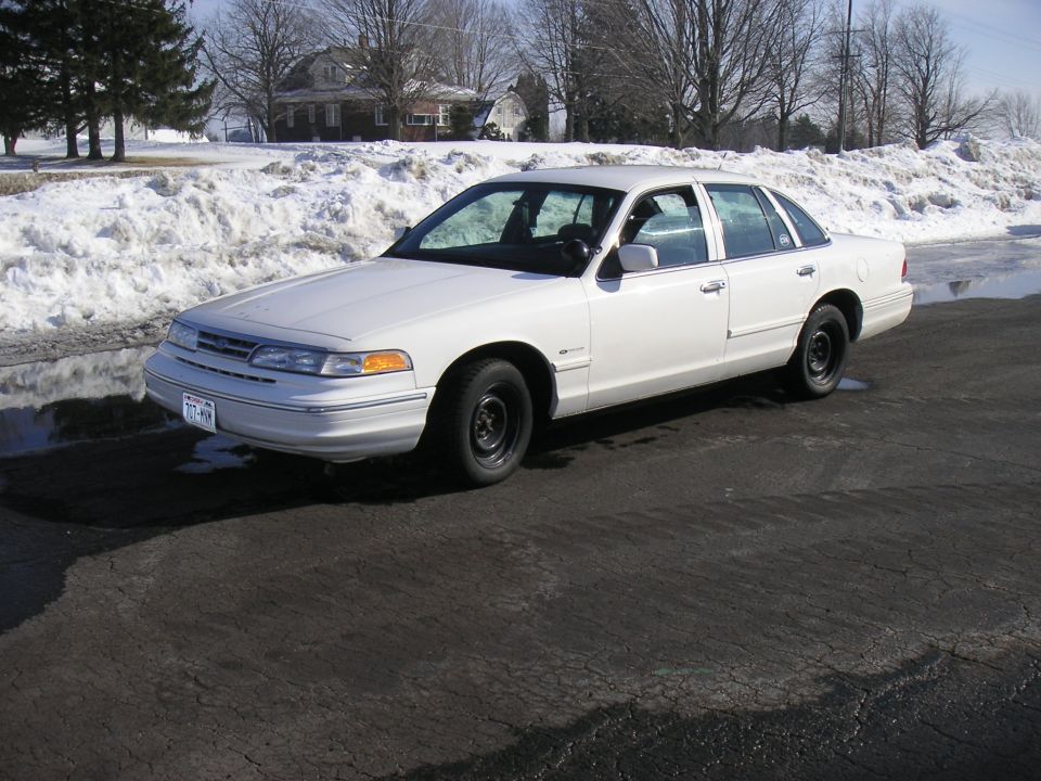 1997 Ford Crown Victoria sedan, white, 3/4 front view, parked on asphalt with snow in background