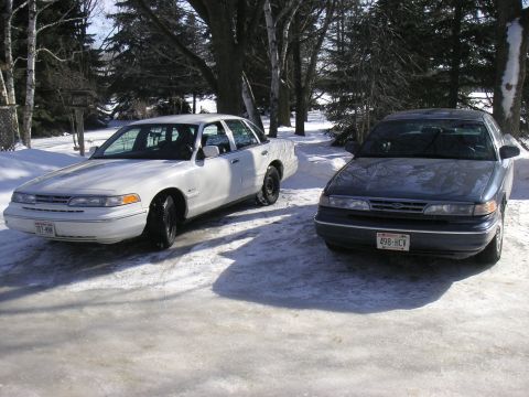 1997 Ford Crown Victoria - Two vehicles sit in the snow, possibly during winter maintenance.