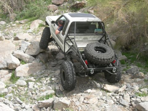 1986 Toyota Hilux - An off-road vehicle tackles a challenging rocky path, its spare tire mounted externally for the journey.