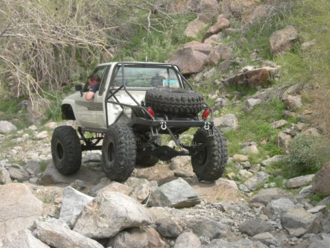 1986 Toyota Hilux - Off-road vehicle navigating a rocky trail with dense foliage in the background.