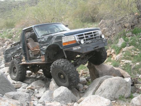 1986 Toyota Hilux - A black pickup truck navigates a rocky terrain, kicking up dust.