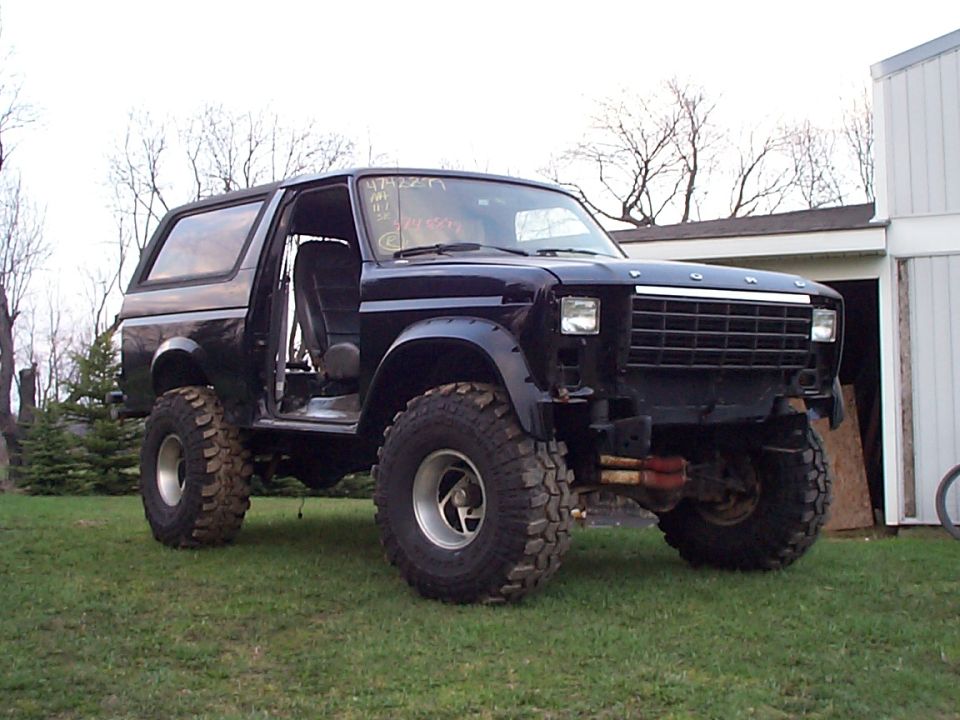 Dark blue lifted Ford Bronco with door removed, mud tires, no front bumper, on grass
