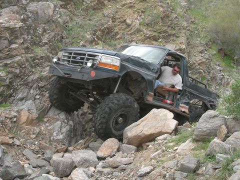 1986 Toyota Hilux - A modified Ford F-Series truck navigates a rocky trail with a driver inside.