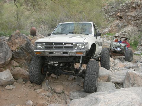 1986 Toyota Hilux - Two off-road vehicles tackle a challenging rocky path in a desert landscape.