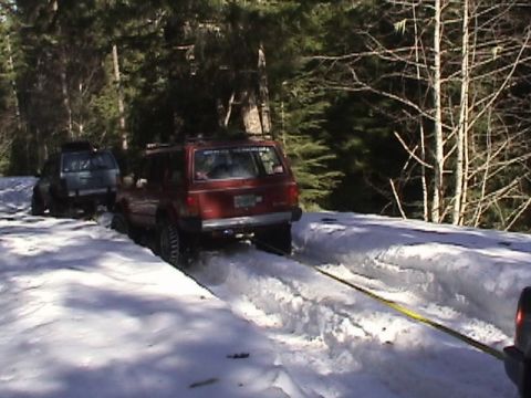 2005 Jeep Wrangler - Two SUVs navigate a snow-covered trail, with one vehicle assisting the other out of a snowy rut.