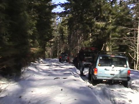 2005 Jeep Wrangler - Rear view of a light blue Jeep XJ Cherokee stopped on a snow-covered forest road with its brake lights on and a roof rack overhead, while a…