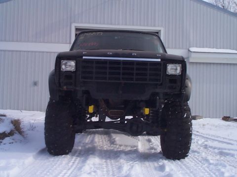 1981 Ford Bronco - A black Ford Bronco sits in the snow, its front end prominently displayed with large tires and visible suspension components.