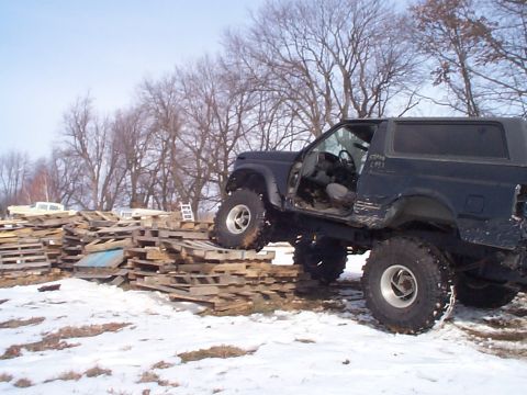 1981 Ford Bronco - A dark SUV with oversized tires is positioned on a stack of wooden pallets in a snowy outdoor setting.