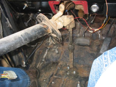 1978 Ford Bronco - The interior of a vehicle shows a rusty floor, steering column, and pedals with exposed wiring.