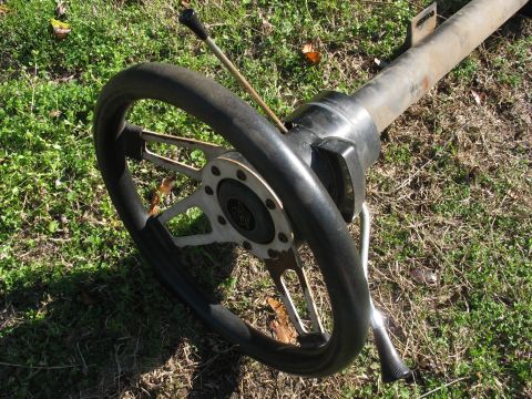 1978 Ford Bronco - A steering column and wheel assembly is shown resting on a grassy surface, with a black rim and silver spokes.