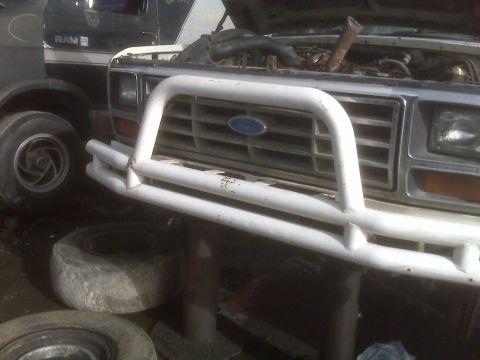 1985 Ford Bronco - Front view of a Ford truck's grille and brush guard, with another vehicle partially visible.