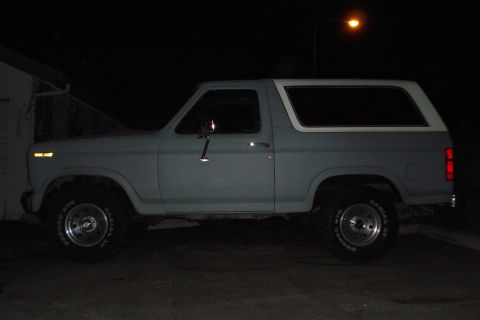 1984 Ford Bronco - This Ford Bronco is parked outside at night, showing its side profile under artificial light.