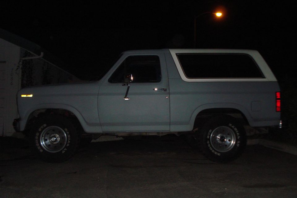 Gray Ford Bronco parked at night, side view. Has a white top and aftermarket wheels
