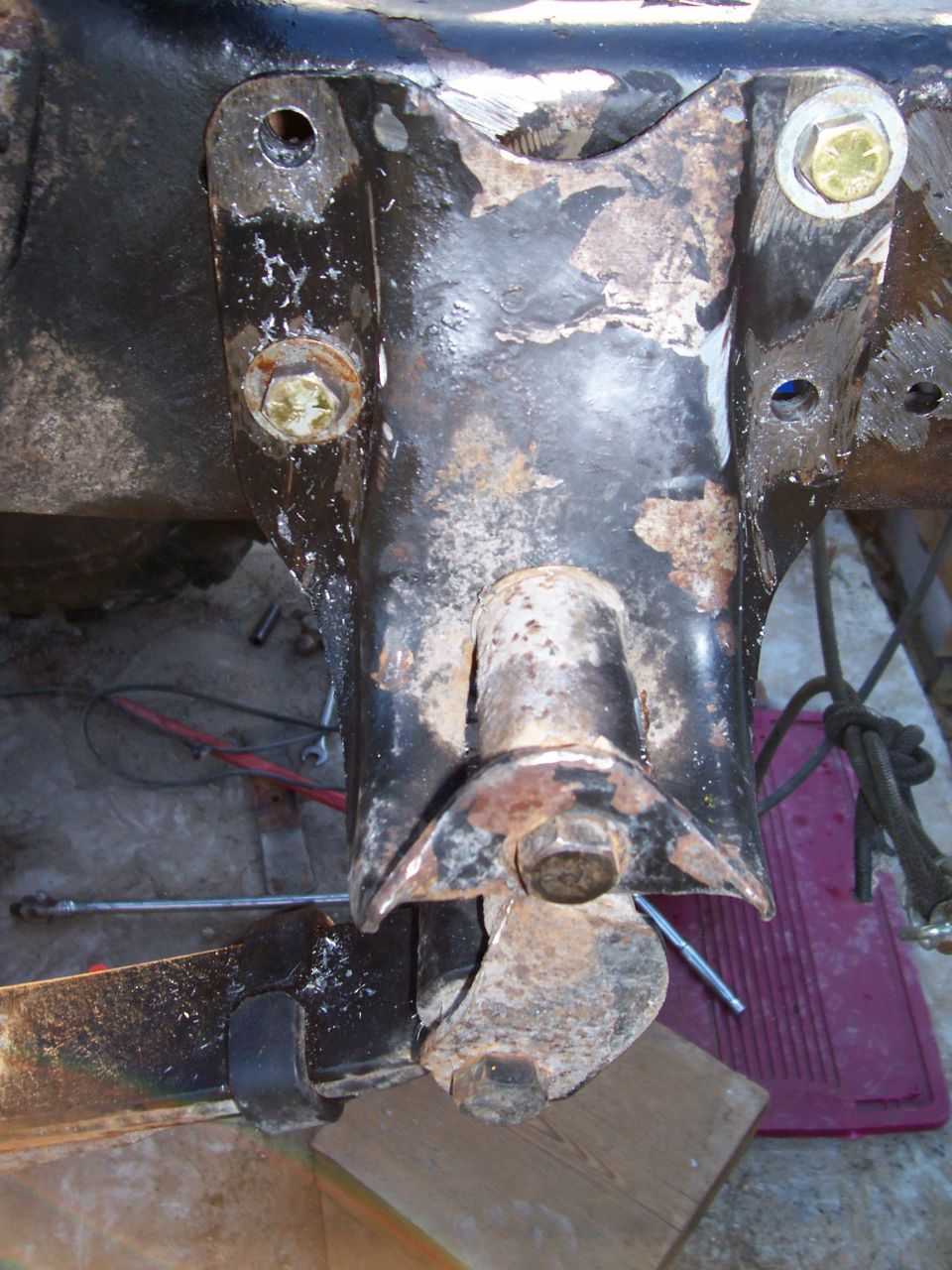 Close-up of a rusty suspension component with bolts and a wooden block underneath