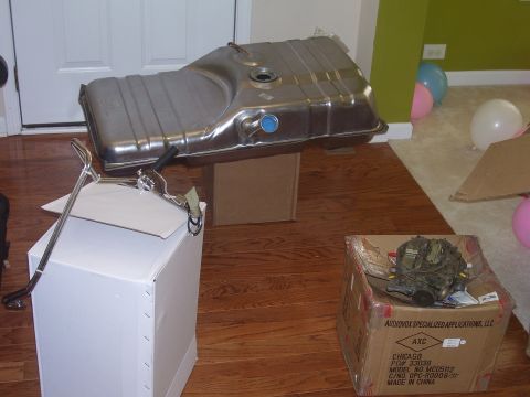 1979 Chevrolet Camaro - A metal fuel tank and a carburetor are displayed on a wooden floor, surrounded by boxes and balloons.