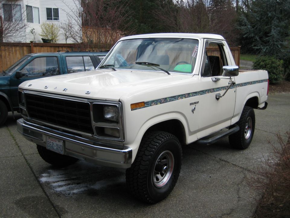 White Ford Bronco parked in driveway next to a dark SUV. License plate reads 652 XHD