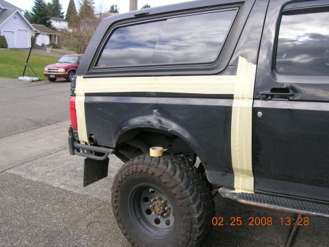 1996 Ford Bronco - A black 1996 Ford Bronco is shown from the side, with masking tape applied to the rear quarter panel, possibly for painting or repair.