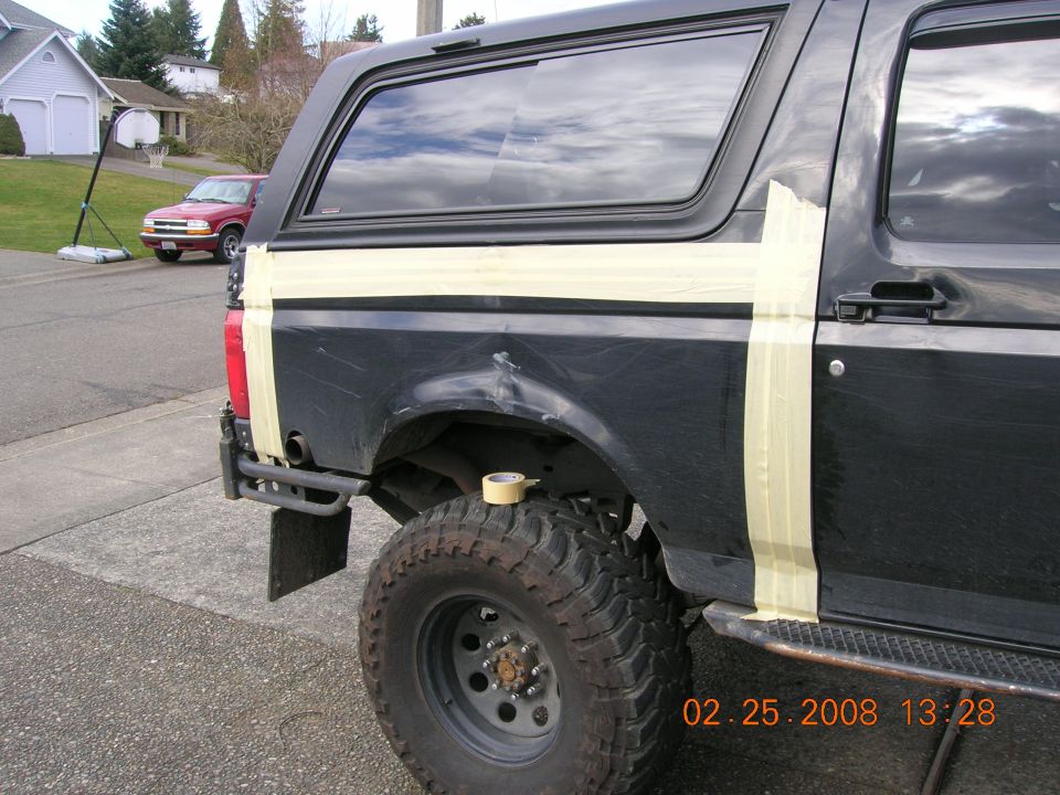 Black lifted Ford Bronco rear quarter masked with tape for repair of a dented panel