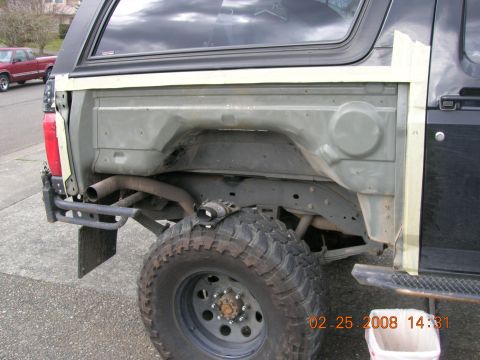 1996 Ford Bronco - Rear fender well of a 1996 Ford Bronco, showing exposed metal and tape. Another vehicle is visible in the background.
