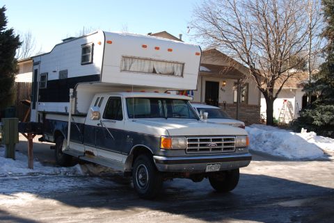 1987 Ford F-250 - A two-tone Ford pickup truck is equipped with a large camper, parked in front of a house on a winter day.