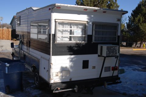 1987 Ford F-250 - A camper van is parked outdoors, showing its rear section with windows and an external air conditioning unit.
