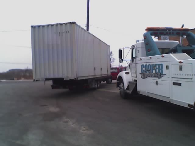 tow truck with 'Cooper Service' logo pulling a large shipping container