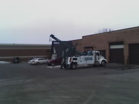 1992 Ford Bronco - A tow truck is parked in front of a commercial building with two other cars nearby.