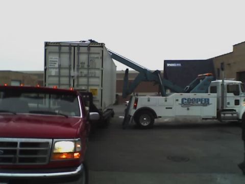 1992 Ford Bronco - A tow truck is seen hauling a large shipping container, with a red truck visible in the foreground.