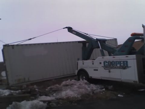 1992 Ford Bronco - A tow truck is actively loading a large shipping container onto a flatbed.