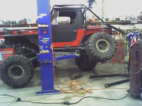 1992 Ford Bronco - A heavily modified off-road vehicle is being worked on in a garage, supported by a hydraulic lift.
