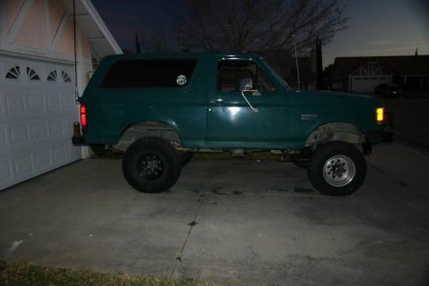 1991 Ford Bronco - Side view of a lifted green 1991 Ford Bronco parked on a concrete driveway.