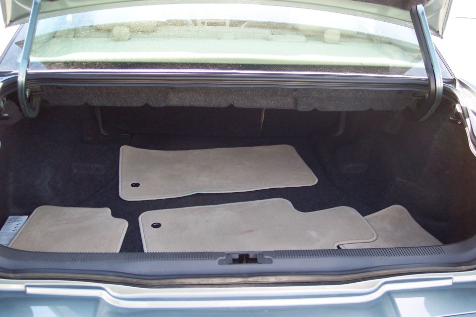 Car trunk interior with four beige floor mats, one partially visible metal object on the left