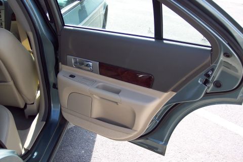 2001 Ford Crown Victoria - The interior door panel features wood trim and beige upholstery, with a view of the rear seat and an adjacent vehicle.