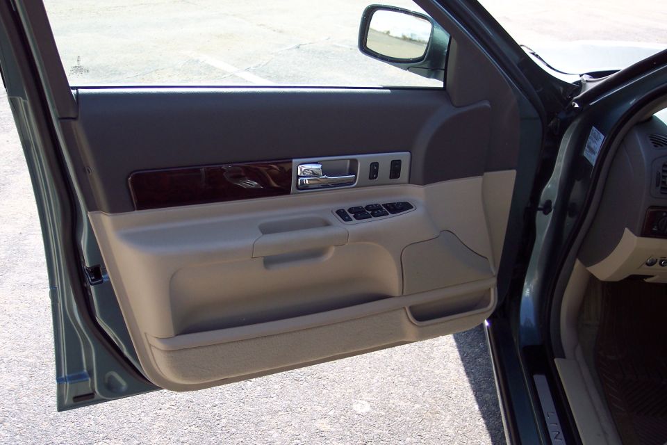 Interior door panel of a car, showing the armrest, door handle, window controls, and wood trim