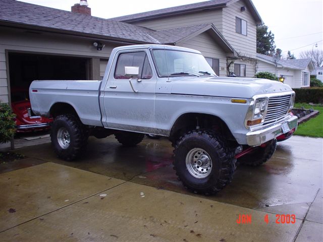 Lifted gray 1970s Ford pickup on large off-road tires in a driveway