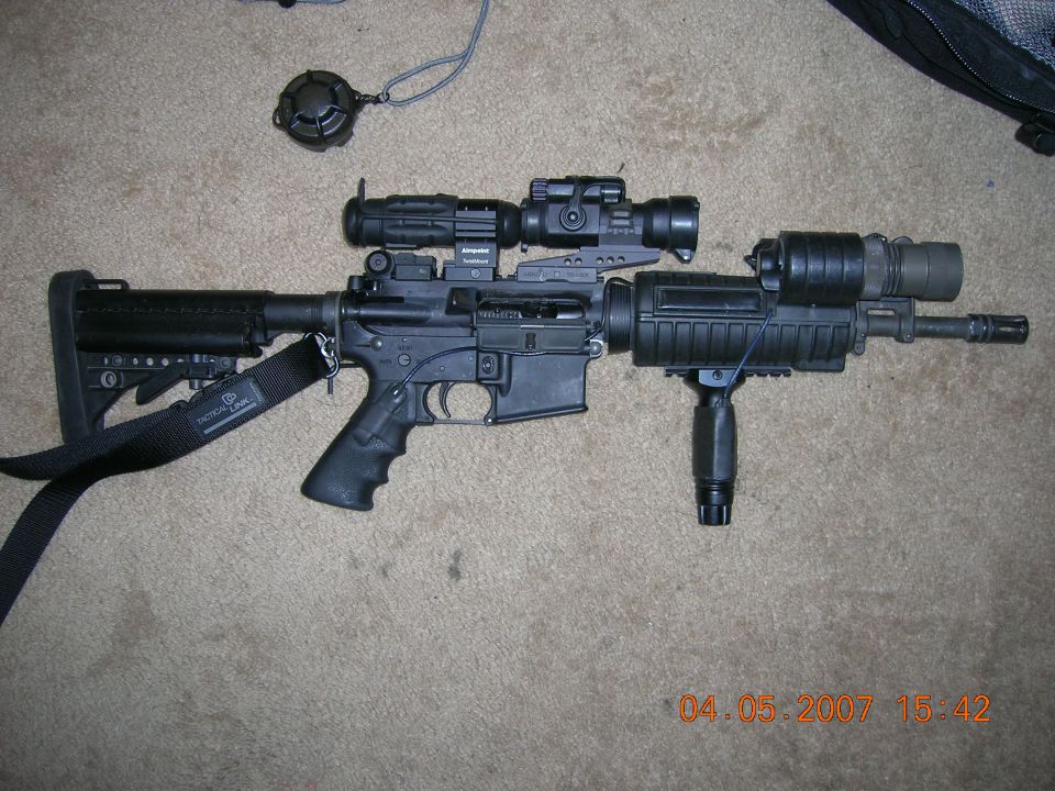 Assault rifle with scope, red dot sight, foregrip, and flashlight mounted on a carpeted surface