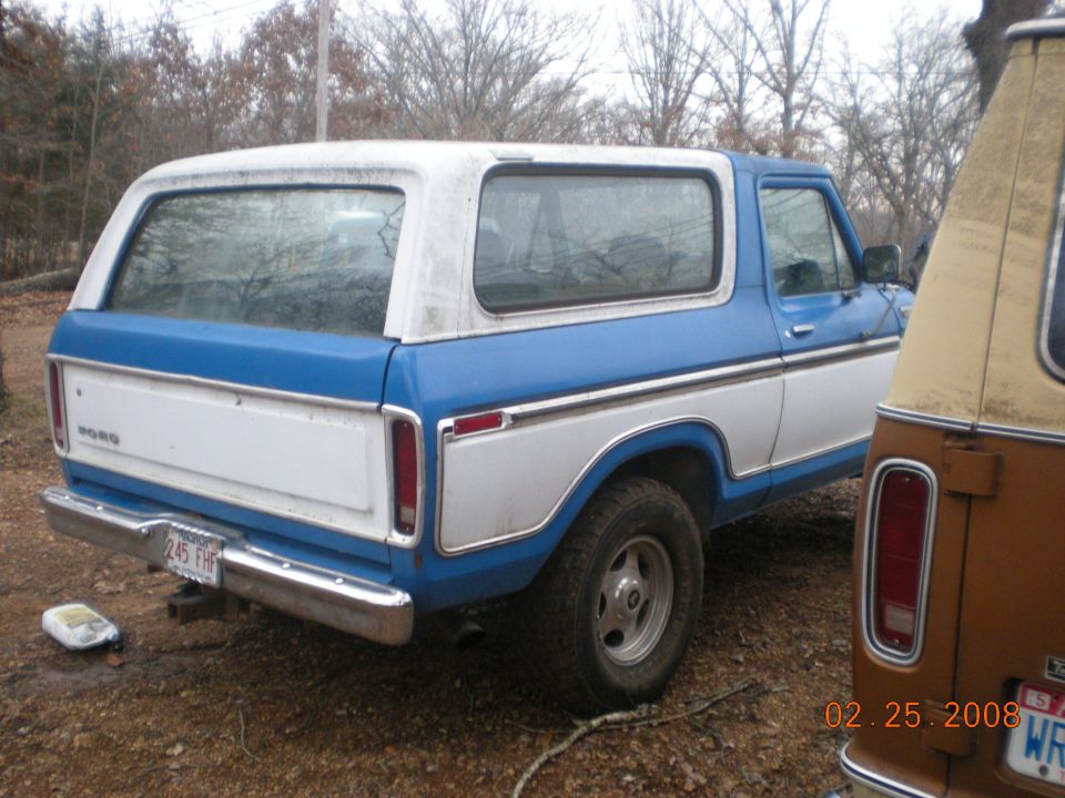 Rear view of a blue and white 1978 Ford Bronco with a brown vehicle to its right