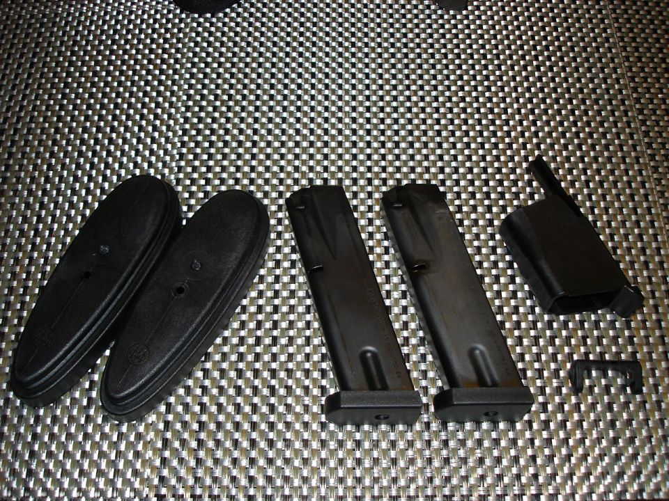 Two rubber recoil pads, two pistol magazines, and small accessories on a woven mesh table