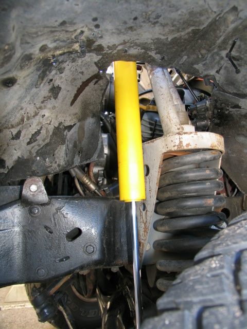 1984 Ford Bronco - Close-up view of the front suspension components, including a yellow shock absorber and a coil spring.