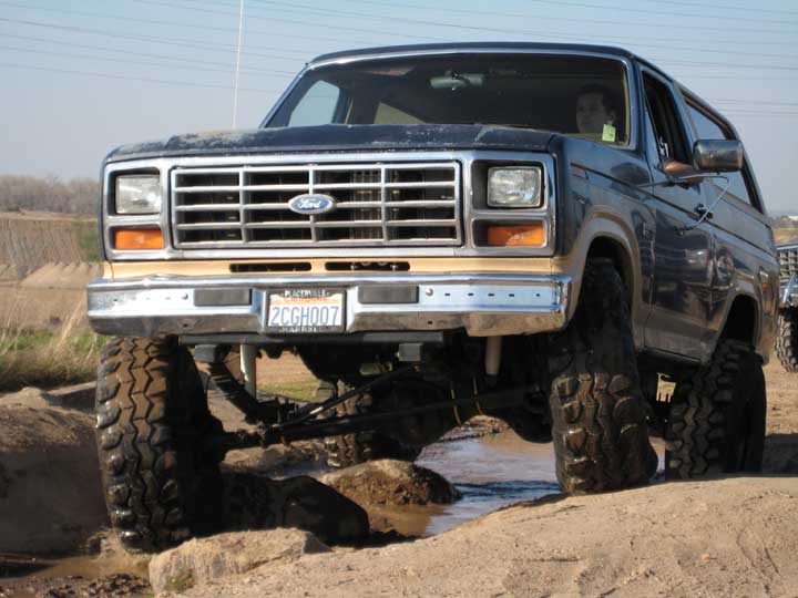 Ford Bronco with lifted suspension driving through mud and rocks. License plate reads 2CGH007