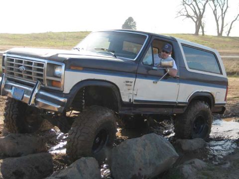 1978 Ford Bronco - A man drives a lifted Ford Bronco through a rocky, muddy terrain.