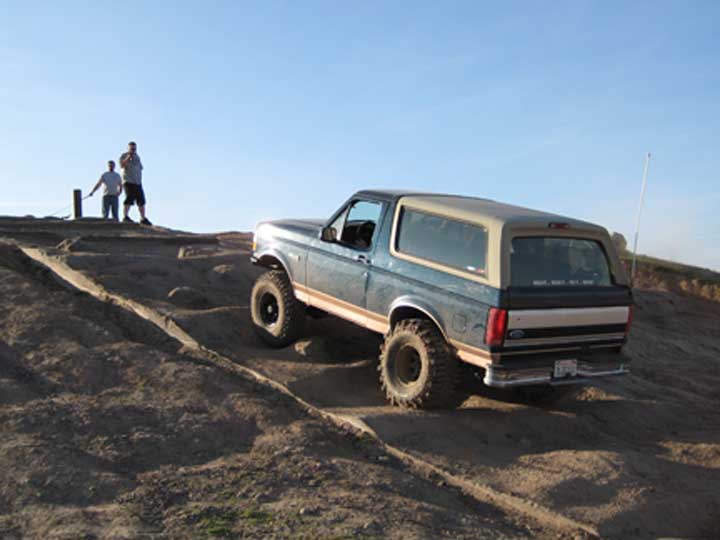 Blue and tan SUV with large tires driving on a dirt hill