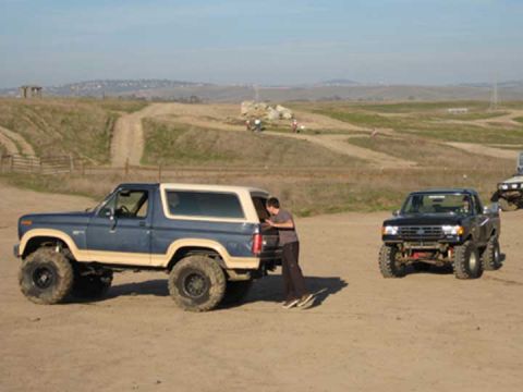 1978 Ford Bronco and a black pickup truck with lifted suspension on a dirt track