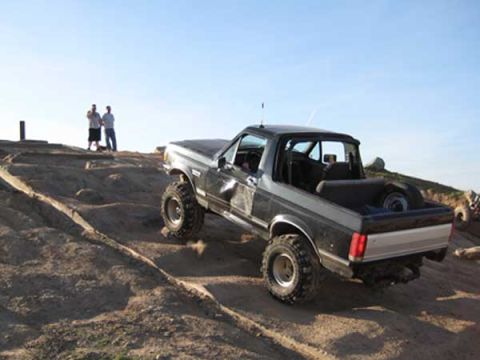 Ford Bronco driving on a dirt hill with two people watching