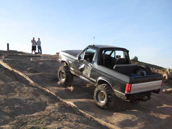 Ford Bronco driving on a dirt hill with two people watching