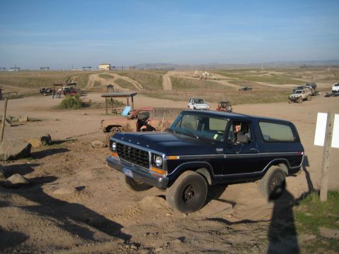 Dark blue 1978 Ford Bronco on a dirt track, front-left wheel elevated