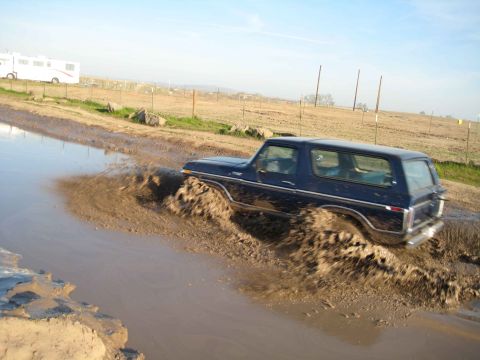 1978 Ford Bronco driving through a muddy puddle, kicking up water