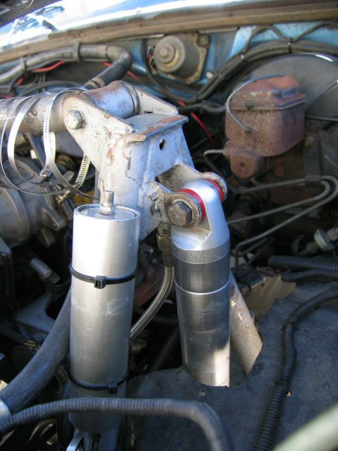 1984 Ford Bronco - This image shows a section of an engine bay, focusing on the brake fluid reservoir and two cylindrical components attached to a bracket.