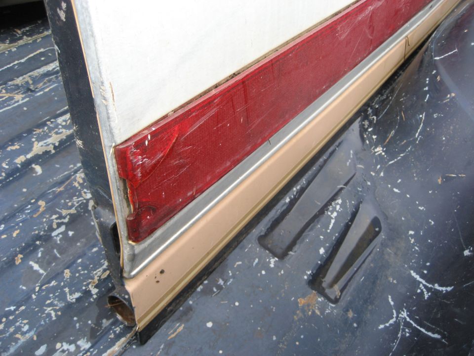 Red tail light and tan trim on a white panel, resting on a dark surface with white paint flecks